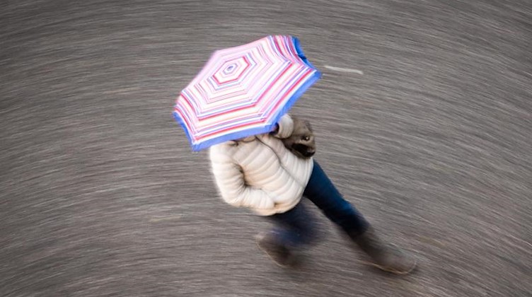 Ein Frau geht bei Regen mit einem Schirm über eine Straße. Foto: Frank Rumpenhorst/dpa/Symbolbild