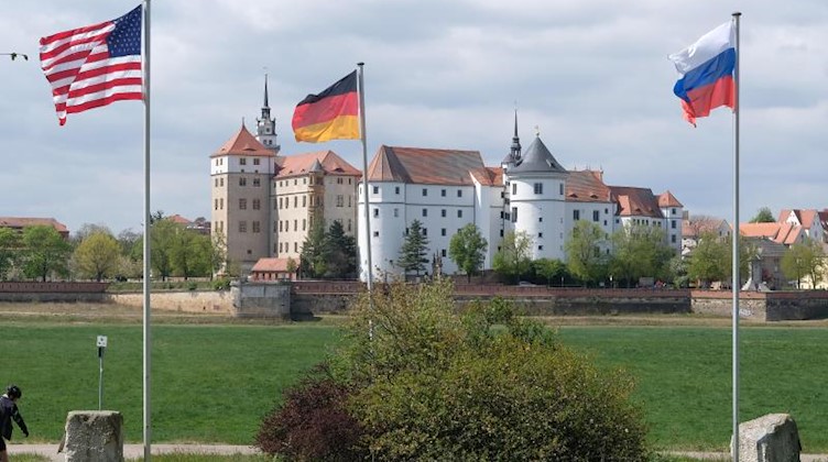 Die US-amerikanische, die deutsche und die russische Fahne am Elbufer, dahinter Schloss Hartenfels. Foto: Sebastian Willnow/dpa-Zentralbild/dpa