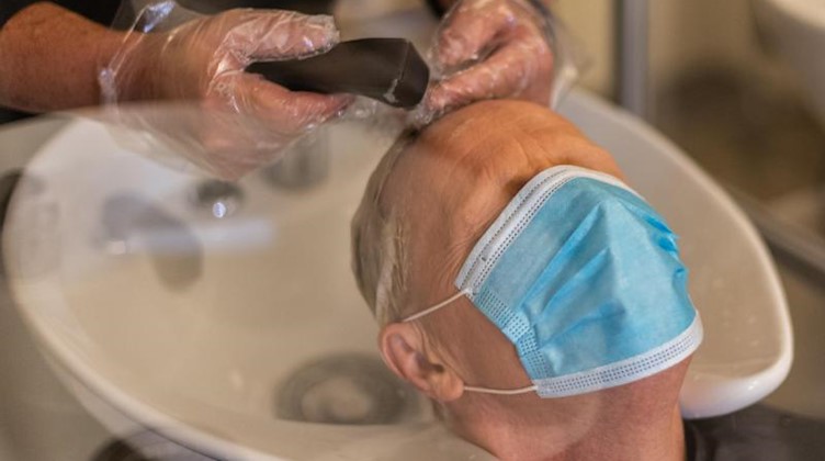 Ein Friseur wäscht einem Kunden in seinem Salon vor dem Schnitt die Haare. Foto: Robert Michael/dpa-Zentralbild/dpa