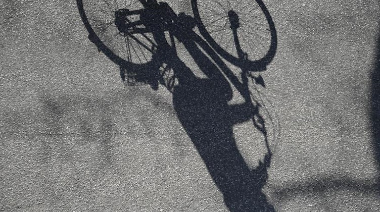 Ein Fahrradfahrer wirft einen langen Schatten auf den Asphalt einer Straße. Foto: Marcus Brandt/dpa/Symbolbild