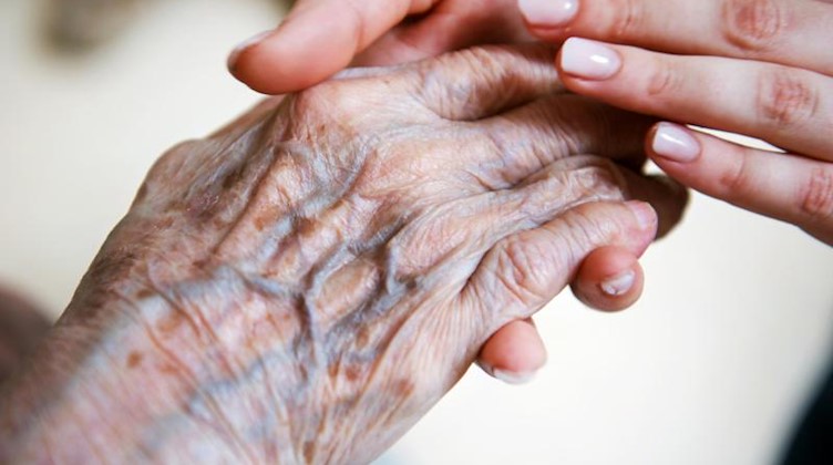Eine Pflegerin hält die Hand einer älteren Frau. Foto: Christophe Gateau/dpa/Illustration/Archivbild