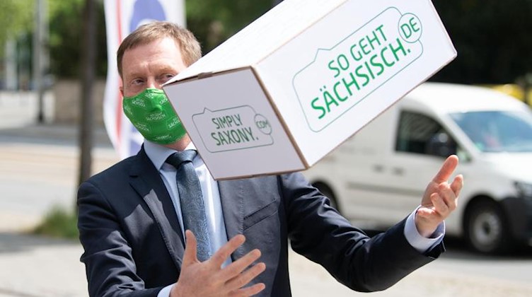 Michael Kretschmer (CDU) mit Mundschutz fängt einen Karton. Foto: Sebastian Kahnert/dpa-Zentralbild/dpa
