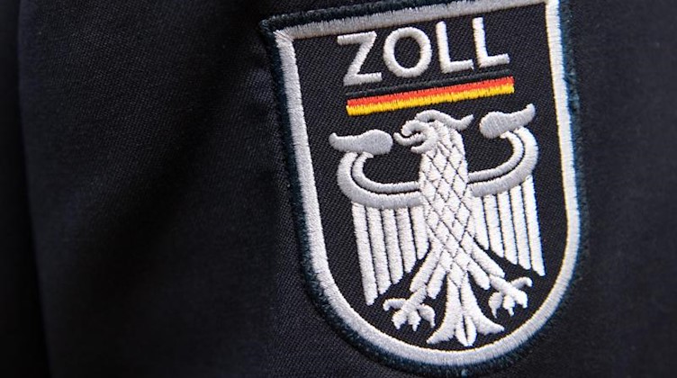 Das Logo der deutschen Zollbehörde ist an einer Uniform zu sehen. Foto: Ralf Hirschberger/dpa/Symbolbild
