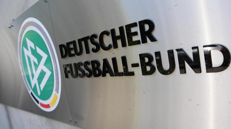DFB-Logo und Schriftzug sind vor der Zentrale des Deutschen Fußball-Bundes (DFB) an einer Mauer platziert. Foto: Arne Dedert/dpa/Archivbild