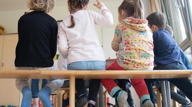 Kinder sitzen in einem Kindergarten auf einer Bank nebeneinander. Foto: Sebastian Kahnert/dpa-Zentralbild/dpa/Archivbild