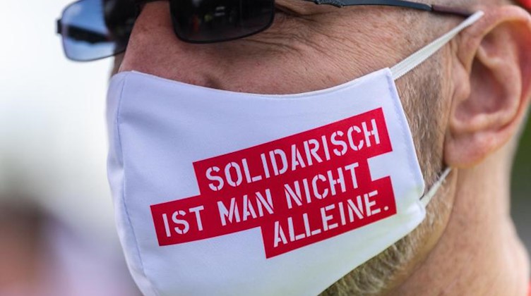 Ein Teilnehmer an einem Warnstreik vor dem Werkstor des Dresdner Chiphersteller Globalfoundries trägt einen Mundschutz mit der Aufschrift "Solidarisch ist man nicht alleine". Foto: Robert Michael/dpa-Zentralbild/dpa
