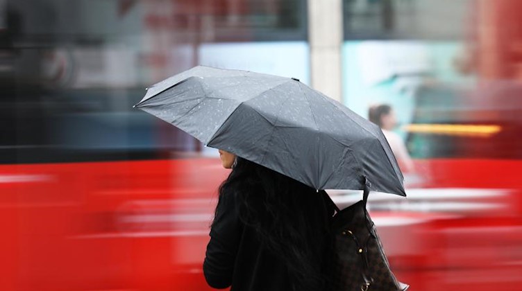 Eine Frau steht mit einem Regenschirm an einer Straße. Foto: Oliver Berg/dpa/Symbolbild