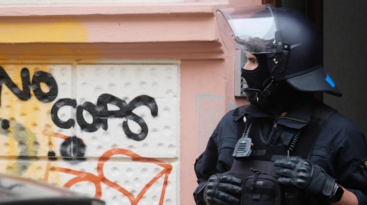 Ein Polizist steht vor einem Hauseingang in Connewitz auf dem an der Wand "No Cops" (Keine Polizisten) steht. Foto: Sebastian Willnow/dpa-Zentralbild/dpa