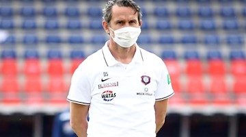 Dirk Schuster steht mit Maske vor dem Spiel im Stadion. Foto: Tom Weller/dpa-Pool/dpa/Archivbild