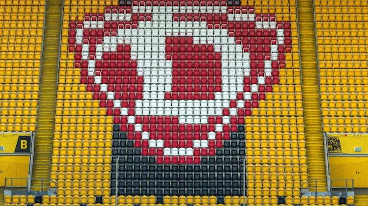 Das Logo von Dynamo Dresden ist auf der Tribüne auf gelben und schwarzen Sitzen zu sehen. Foto: Robert Michael/dpa-Zentralbild/dpa/Archivbild