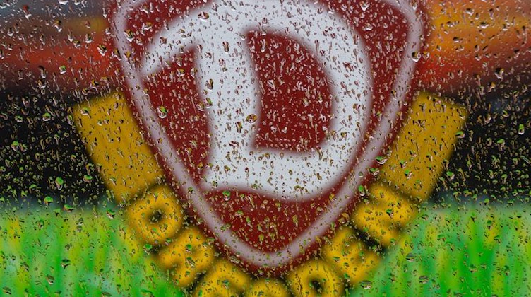 Das Logo des Fußball-Zweitligisten SG Dynamo Dresden ist hinter Regentropfen zu sehen. Foto: Robert Michael/dpa-Zentralbild/dpa/Archivbild