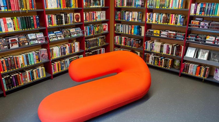 Ein rotes, geschwungenes Sofa steht inmitten der Jugendbuchabteilung einer Stadtbibliothek. Foto: Klaus-Dietmar Gabbert/dpa/Archivbild