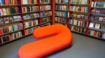 Ein rotes, geschwungenes Sofa steht inmitten der Jugendbuchabteilung einer Stadtbibliothek. Foto: Klaus-Dietmar Gabbert/dpa/Archivbild