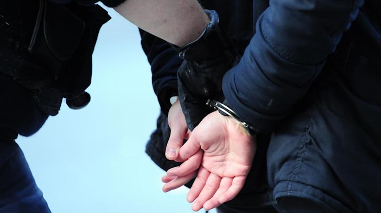 Ein Mann wird in Handschellen abgeführt. Foto: Daniel Reinhardt/dpa/Symbolbild