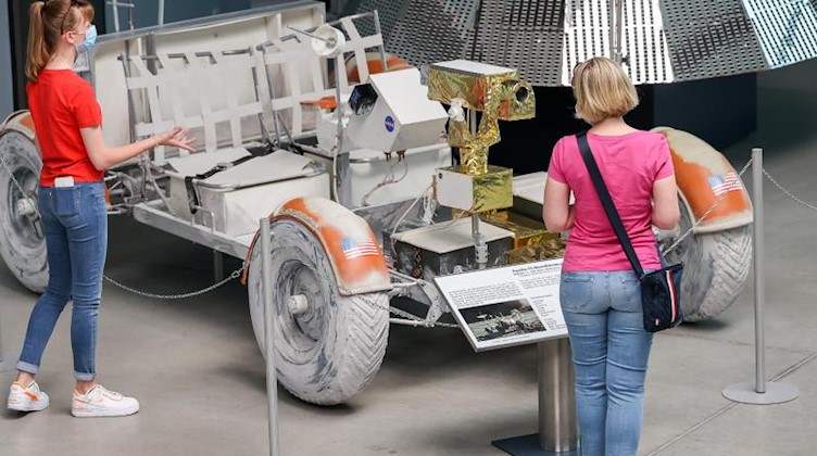 Besucherinnen der Deutschen Raumfahrtausstellung stehen an einem Modell des Lunar Rovers. Foto: Jan Woitas/dpa-Zentralbild/dpa