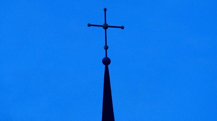 Ein Kreuz ist auf einer Kirchturmspitze zu sehen. Foto: Friso Gentsch/dpa/Symbolbild