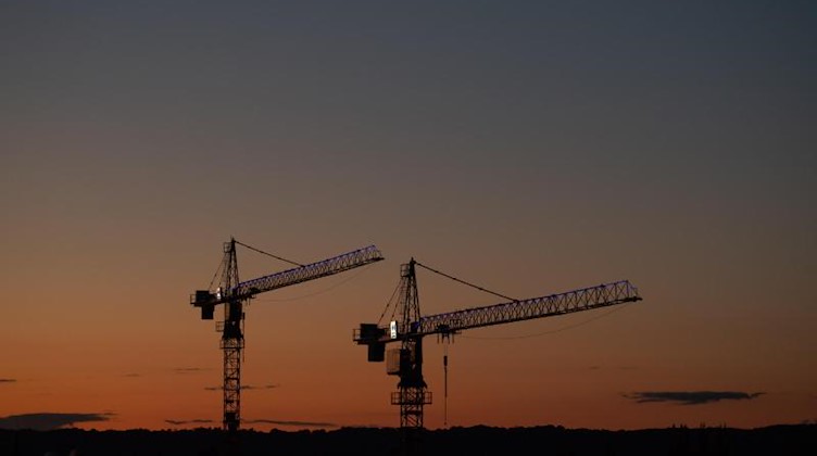 Kräne stehen vor dem Abendhimmel auf einer Baustelle. Foto: Robert Michael/dpa-Zentralbild/ZB/Symbolbild