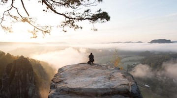 Mann hockt im Nationalpark Sächsische Schweiz auf Basteifelsen und fotografiert Sonnenaufgang. Foto: Sebastian Kahnert/dpa-Zentralbild/dpa