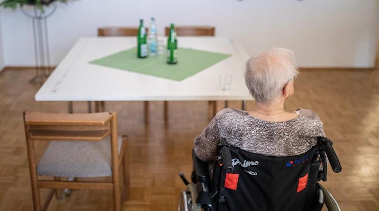 Eine ältere Frau sitzt in einem Pflegeheim in ihrem Rollstuhl vor einem Tisch. Foto: Marcel Kusch/dpa/Symbolbild