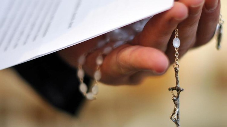 Ein Priester hält einen Rosenkranz und eine bischöfliche Erklärung in der Hand. Foto: picture alliance / dpa