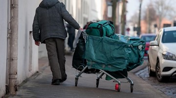 Ein obdachloser Mann schiebt einen Einkaufswagen, samt Planen, Rucksack und Tasche durch die Stadt. Foto: Philipp Schulze/dpa/Archivbild