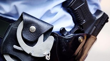 Ein Polizist mit Handschellen und Pistole am Gürtel. Foto: picture alliance / dpa/Archiv