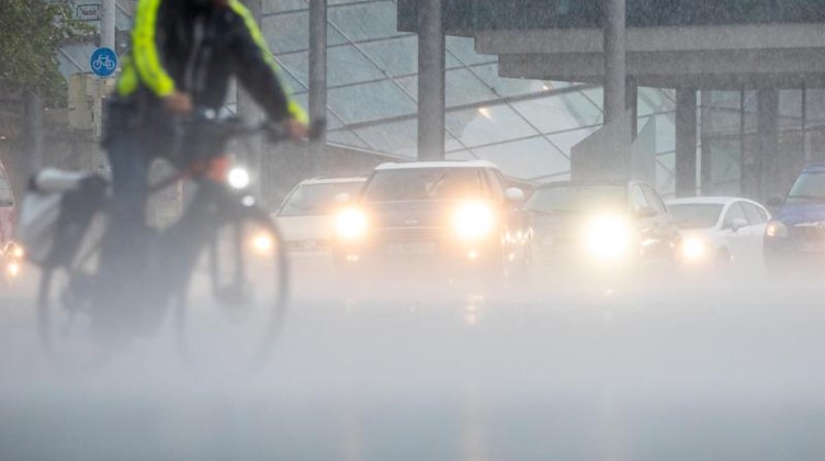 Autos und ein Radfahrer fahren bei Starkregen über die Straße. Foto: Moritz Frankenberg/dpa/Symbolbild