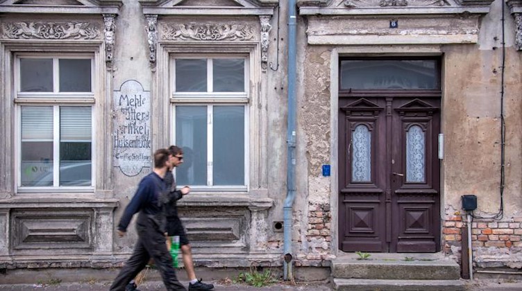 Zwei Männer gehen an einem leerstehenden ehemaligen Wohn- und Geschäftshaus vorbei. Foto: Jens Büttner/dpa-Zentralbild/ZB/Symbolbild