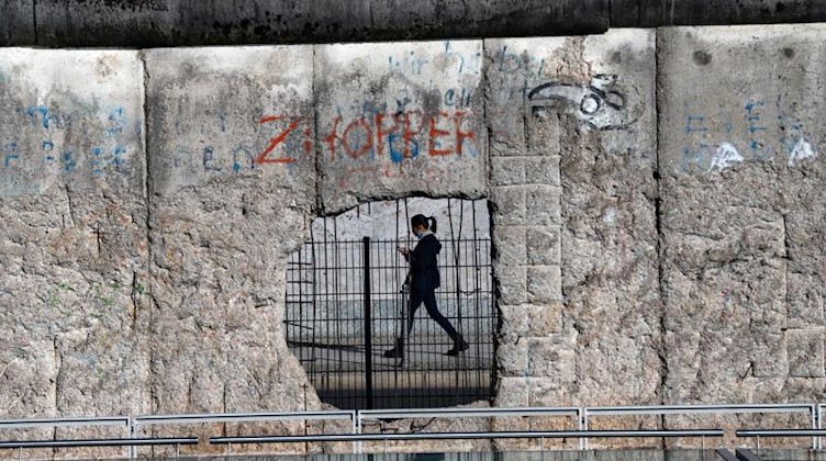 Eine Frau ist durch ein Loch der ehemaligen Berliner Grenzmauer an der Niederkirchnerstraße zu sehen. Foto: Paul Zinken/dpa-Zentralbild/dpa/Archivbild