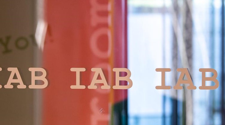 Das Buchstaben-Logo vom Institut für Arbeitsmarkt- und Berufsforschung der Bundesagentur für Arbeit, IAB, steht mehrfach auf einer Glasscheibe. Foto: Daniel Karmann/dpa/Archivbild