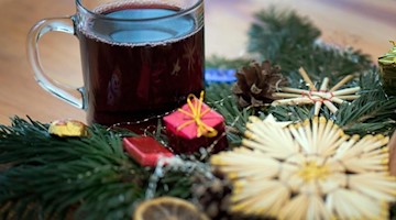 Ein Glas roter Glühwein neben einem Weihnachtsgesteck. Foto: Arno Burgi/dpa-Zentralbild/dpa/Symbolbild