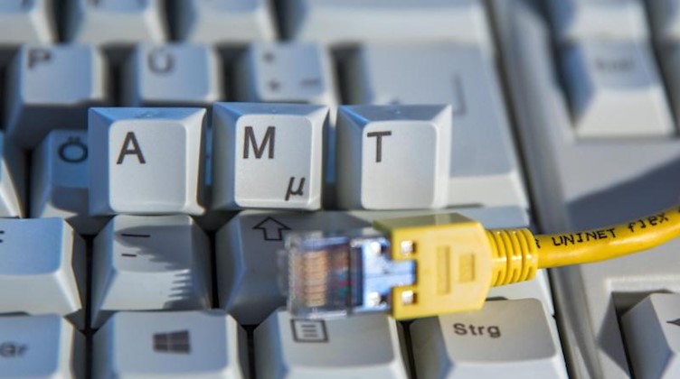 Der Schriftzug «Amt» ist auf einer Computertastatur hinter einem Netzwerkkabel zu sehen. Foto: Jens Büttner/dpa-Zentralbild/ZB/Illustration