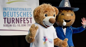 Die Maskottchen des Turnfestes (l) und der Messe Leipzig stehen auf einer Bühne. Foto: picture alliance / Rainer Jensen/dpa/Symbolbild