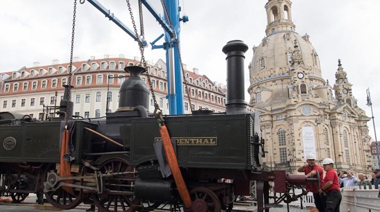 Mitarbeiter der Firma DB Schenker heben vor der Frauenkirche die historische Dampflokomotive «Muldenthal» mit einem Kran von einem Gleis. Foto: Sebastian Kahnert/dpa-Zentralbild/dpa/Archiv