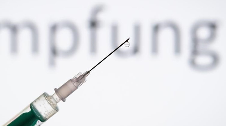 Eine Spritze wird vor den Schriftzug «Impfung» gehalten. Foto: Friso Gentsch/dpa