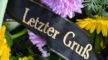 Eine Trauerschleife mit der Aufschrift «Letzter Gruß» auf einem Grab. Foto: Patrick Pleul/dpa-Zentralbild/dpa/Symbolbild