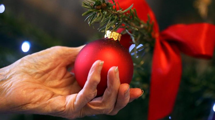 Eine ältere Dame hält in einem Seniorenheim eine rote Christbaumkugel in ihrer Hand. Foto: picture alliance / dpa/Illustration