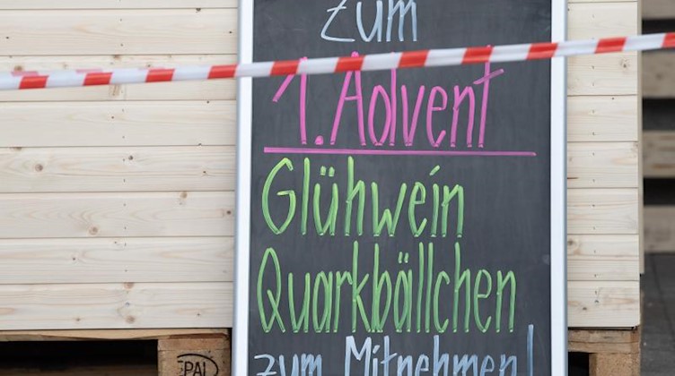 Ein Absperrband hängt vor einer Tafel mit der Aufschrift «Zum 1. Advent Glühwein Quarkbällchen zum Mitnehmen». Foto: Sebastian Kahnert/dpa-Zentralbild/dpa/Symbolbild