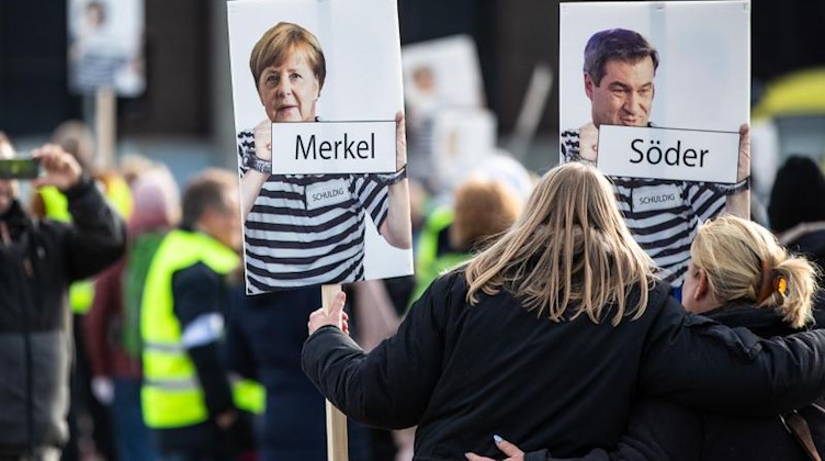 Bundeskanzlerin Merkel (CDU) und Bayerns Ministerpräsident Söder (CSU) in «Sträflingskleidung» sind auf Schildern zweier Frauen während einer Demonstration zu sehen, die sich gegen die Corona-Politik der Bundesregierung richtet. Foto: Christoph Schmidt/dpa/Archivbild