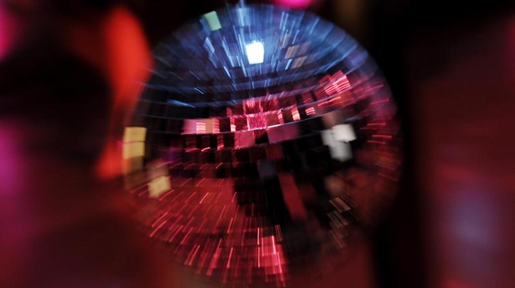 Scheinwerferlicht spiegelt sich in einer Discokugel. Foto: picture alliance / dpa/Symbolbild