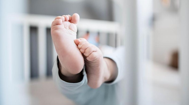 Die Füße eines Babys sind in einem Kinderbett zu sehen. Foto: Fabian Strauch/dpa/Illustration