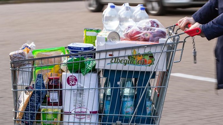 Ein Einkaufswagen mit Lebensmitteln wird über den Parkplatz eines Supermarkts geschoben. Foto: Jens Büttner/dpa-Zentralbild/dpa/Symbolbild