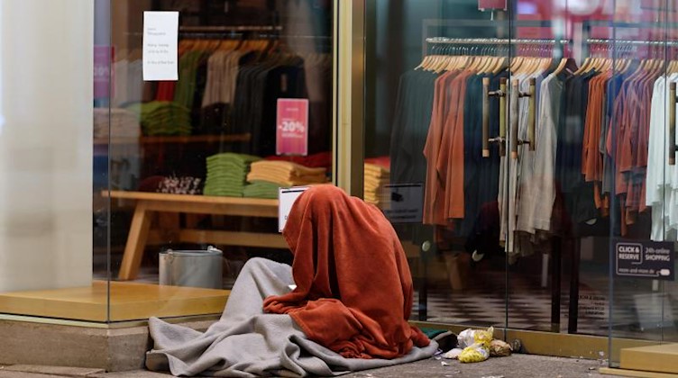 Ein Mann sitzt in der Innenstadt in einem Schlafsack im Eingang zu einem Geschäft. Foto: Henning Kaiser/dpa/Archivbild
