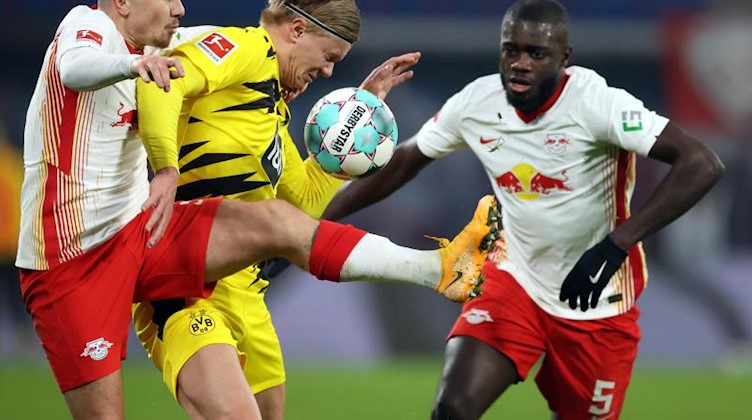 Leipzigs Angelino (l) und Dayot Upamecano kämpfen mit Dortmunds Erling Haaland um den Ball. Foto: Jan Woitas/dpa