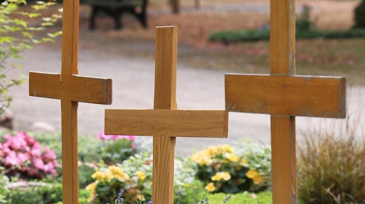 Drei Holzkreuze stehen auf einem Friedhof. Foto: Sebastian Willnow/dpa-tmn/Symbolbild