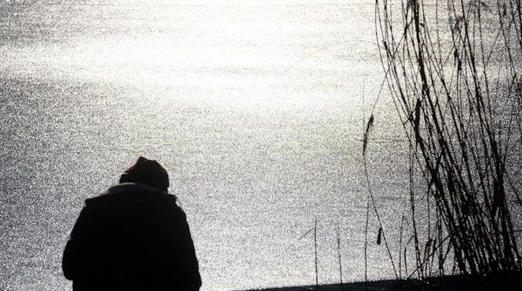 Ein Mann sitzt an einem zugefrorenen Teich im Agra-Park südlich von Leipzig in der Sonne. Foto: Sebastian Willnow/dpa-Zentralbild/dpa/Archivbild