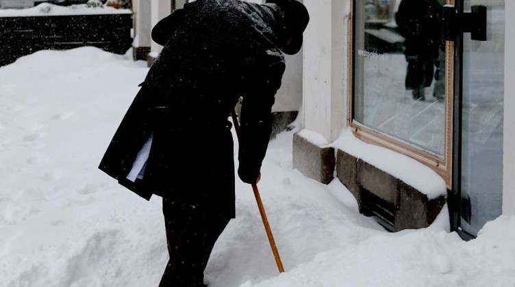 Ein Mann räumt Schnee vor einem Ladengeschäft. Foto: Sebastian Willnow/dpa-Zentralbild/dpa