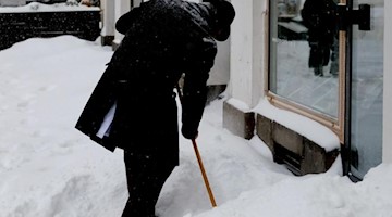 Ein Mann räumt Schnee vor einem Ladengeschäft. Foto: Sebastian Willnow/dpa-Zentralbild/dpa