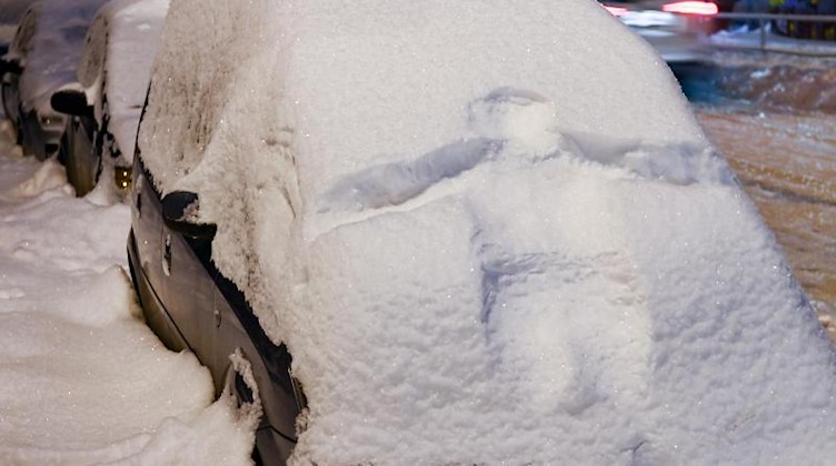 Der Abdruck einer Person ist in der schneebedeckten Front eines Autos zu sehen. Foto: Hendrik Schmidt/dpa-Zentralbild/dpa