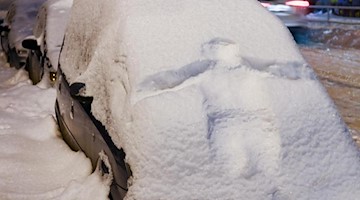 Der Abdruck einer Person ist in der schneebedeckten Front eines Autos zu sehen. Foto: Hendrik Schmidt/dpa-Zentralbild/dpa